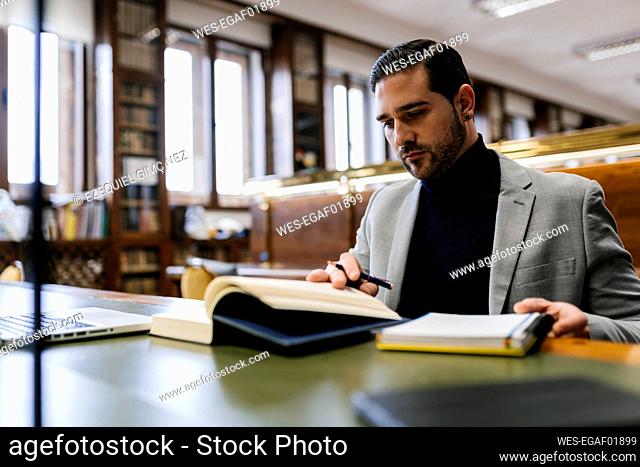 Businessman with laptop reading book while working in library