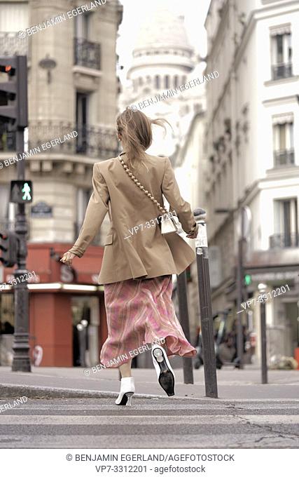 fashionable blogger woman running at street towards touristic sight Basilica Sacré-Cœur, during fashion week, in city Paris, France