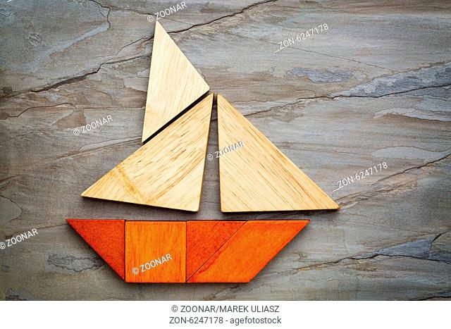abstract picture of a sailing boat built from seven tangram wooden pieces over a slate rock background, travel or vacation concept
