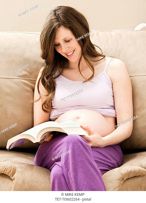 USA, Utah, Lehi, Young pregnant woman sitting on sofa, reading book