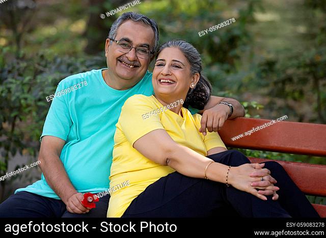 A SENIOR COUPLE HAPPILY LAUGHING WHILE SITTING ON A PARK BENCH