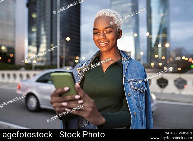 Smiling woman using smart phone on bridge in city at dusk