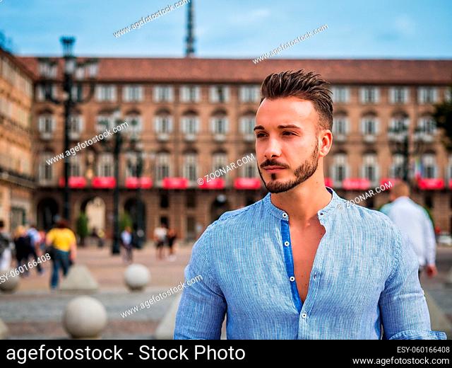 One handsome young man in urban setting in European city, standing, wearing shirt