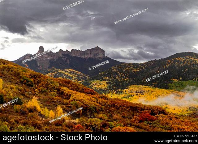 Mountain valley of changing yellow aspen trees and orange scrub in valley in front of Courthouse Mountain and Chimney Rock along Owl Creek Pass on stormy fall...