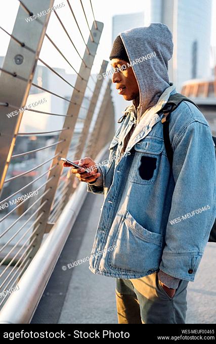 Young man standing on a bridge in the city using smartphone