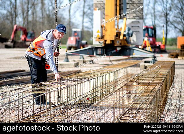 12 April 2022, North Rhine-Westphalia, Hörstel: Henry Heidrich, an apprentice at a construction company, hooks the iron baskets for the foundation onto a crane...
