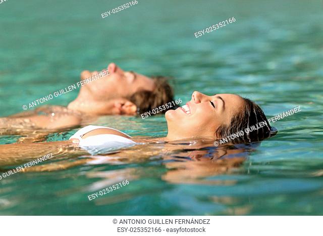 Profile of a couple of tourists swimming in the sea of a tropical resort floating on the turquoise water on summer vacations