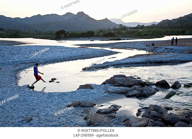 Young woman stepping on a stone in a creek on the beach, beach of Berchidda in the evening light, Berchidda, Siniscola, Sardinia, Italy, Europe