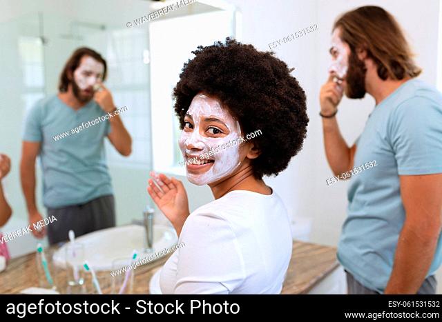 Portrait of happy diverse couple standing in bathroom wearing beauty masks