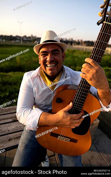 Happy guitarist holding guitar on bench