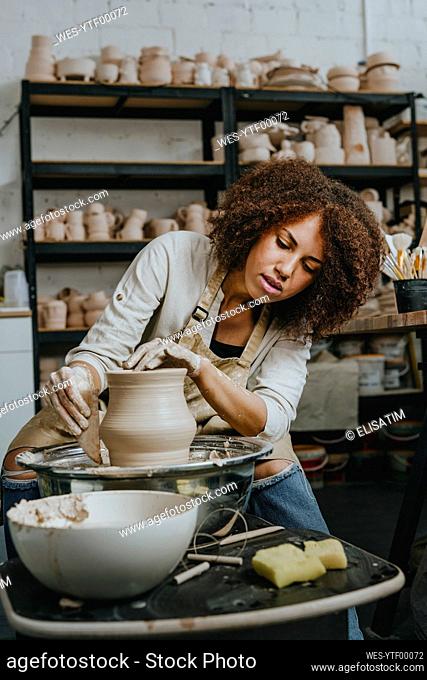 Young craftswoman molding pot shape on pottery wheel