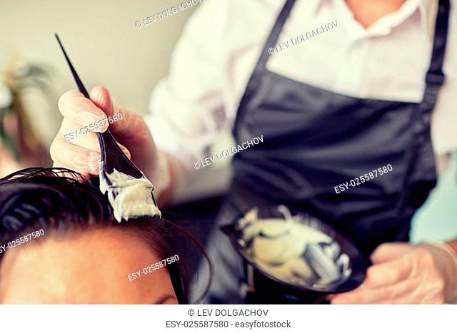 beauty and people concept - close up of stylist with hair dye and brush coloring hair at salon