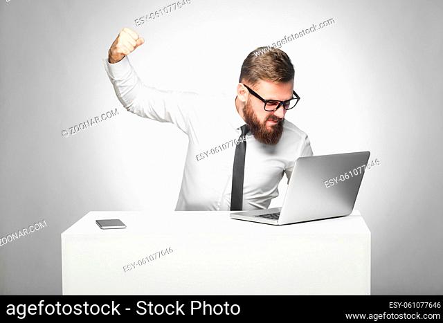 Portrait of aggressive unhappy businessman sitting in office and having bad mood are ready to punch a worker through a webcam with fist and angry face