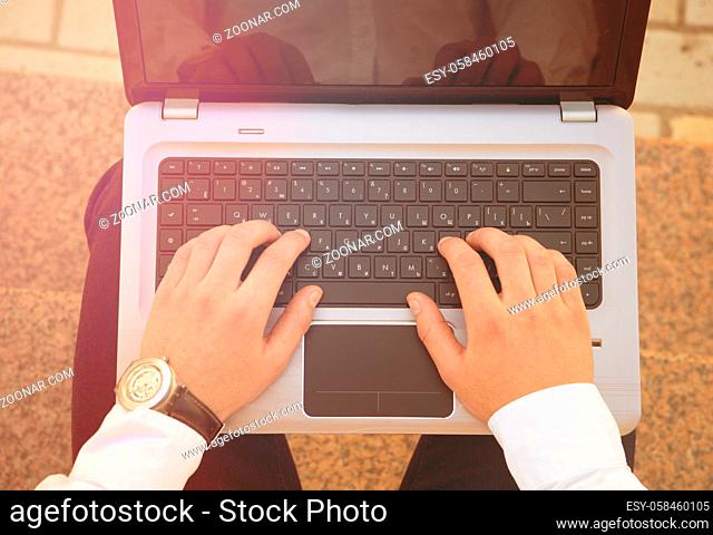 Close-up picture of male hands using computer. Man with beautiful watch on his arm typing the important document outdoors. Toned image