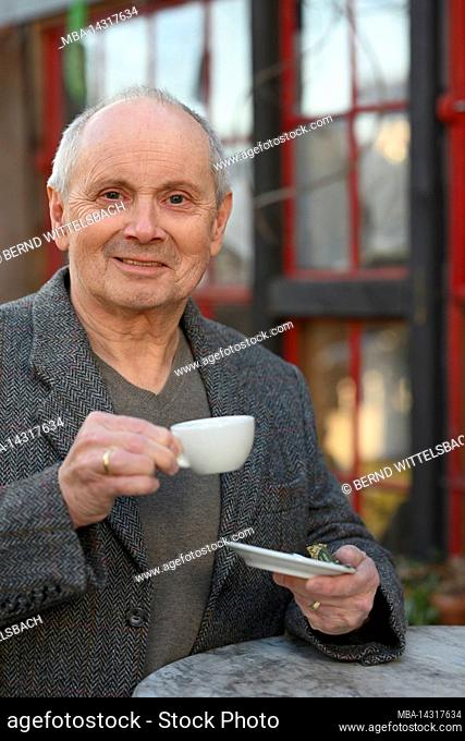 Portrait of smiling gray haired man standing in garden drinking coffee