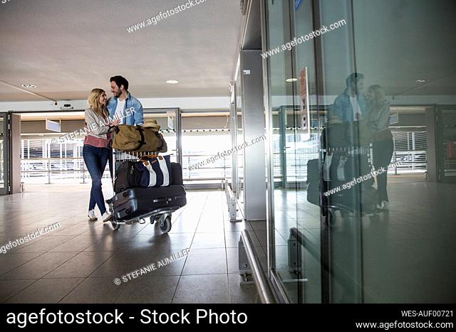 Happy young couple with luggage trolley at airport terminal