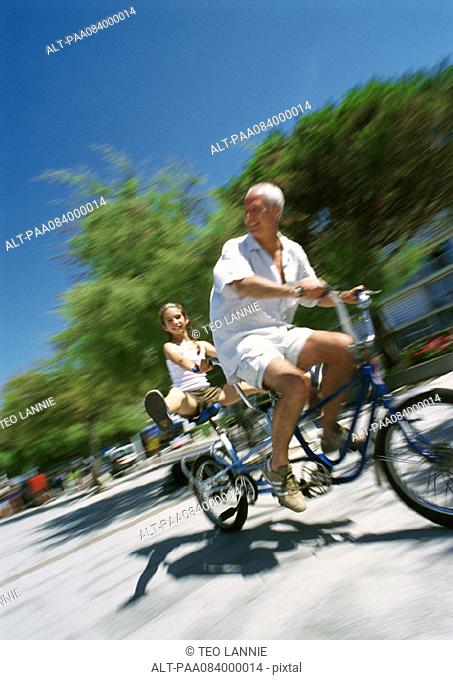 Mature man and girl riding bikes, blurred motion