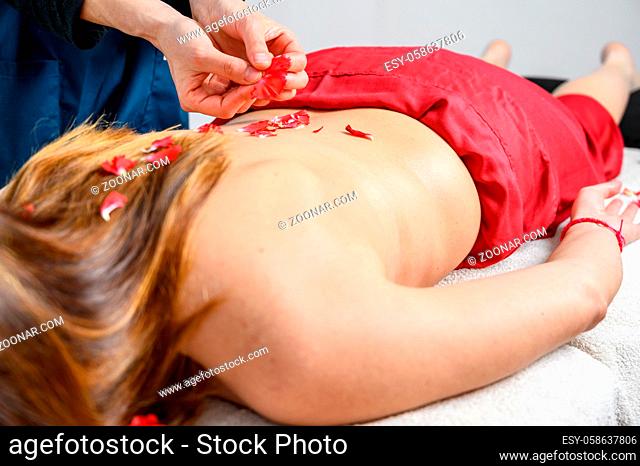 Beautiful woman getting massage and spa treatment with flower petals in spa salon