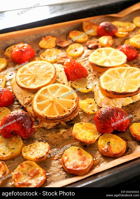 Cod fillet garnished with thyme, garlic and tomatoes, preparation of a healthy dish. Healthy food concept