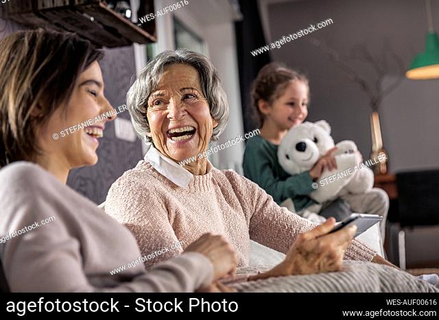Smiling mother looking at daughter with granddaughter in background at home