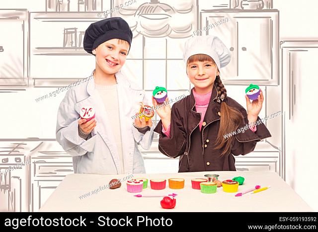 Beautiful boy and girl in chef clothes making christmas cupcakes. Children standing over kitchen drawing background