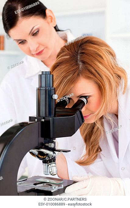 Cute scientist looking through a microscope with her assistant