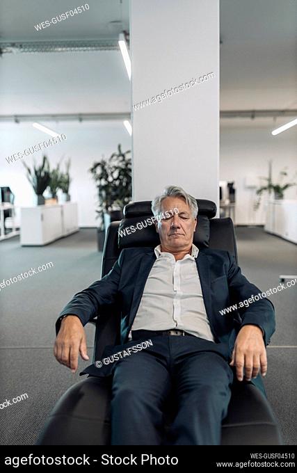 Businessman with eyes closed relaxing on arm chair at office