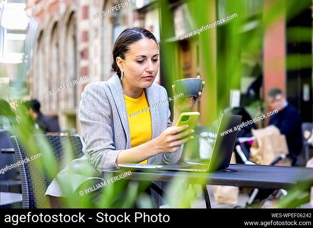 Businesswoman holding coffee cup using smart phone at sidewalk cafe