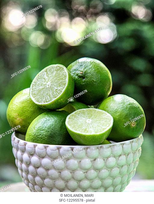 Fresh limes, whole and halved, in a ceramic bowl