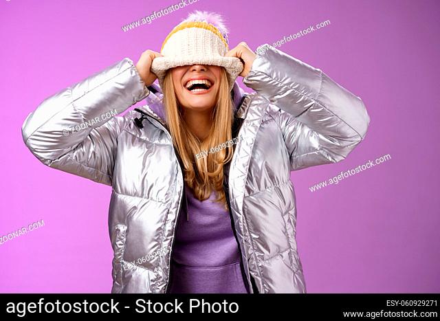 Lifestyle. Delighted carefree charming happy young blond woman having fun hiding face pulling hat eyes smiling laughing joyfully enjoying winter sunny day...