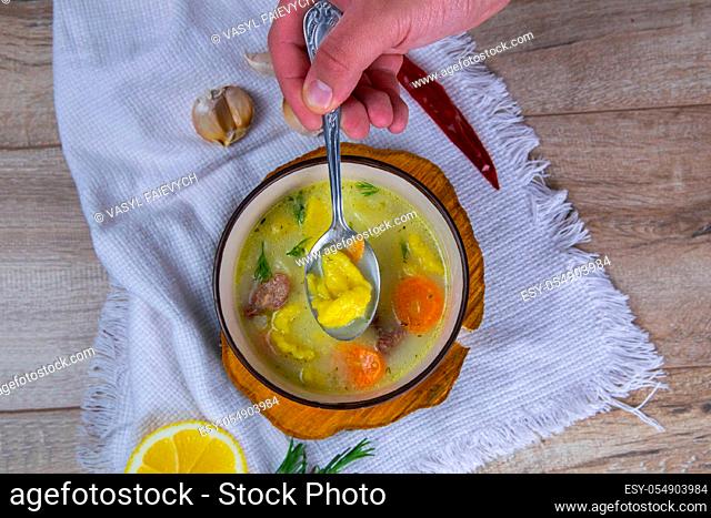 Hand takes a spoonful of soup .Potato cream soup with mushrooms, carrots and cheese. Top view. Soup in a brown plate, stands on a wooden stand, next to a hour