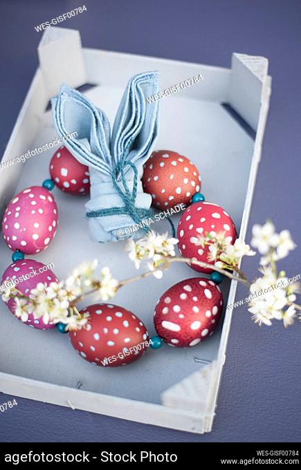 Blossoming twigs, napkin folded into shape of rabbit ears and wreath made of red spotted Easter eggs