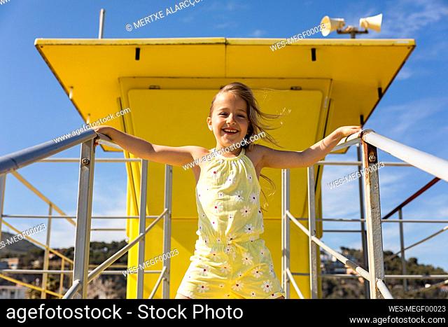 Cheerful girl standing in front of yellow lifeguard hut on sunny day