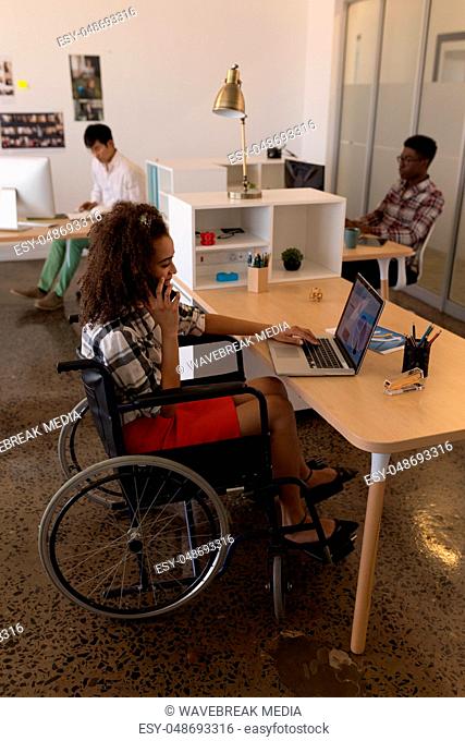 Disabled female executive using laptop while talking on mobile phone at desk