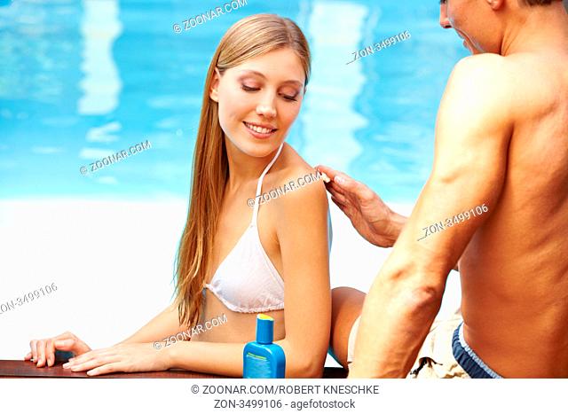 Junger Mann cremt attraktiver Frau im Pool den Rücken mit Sonnencreme ein