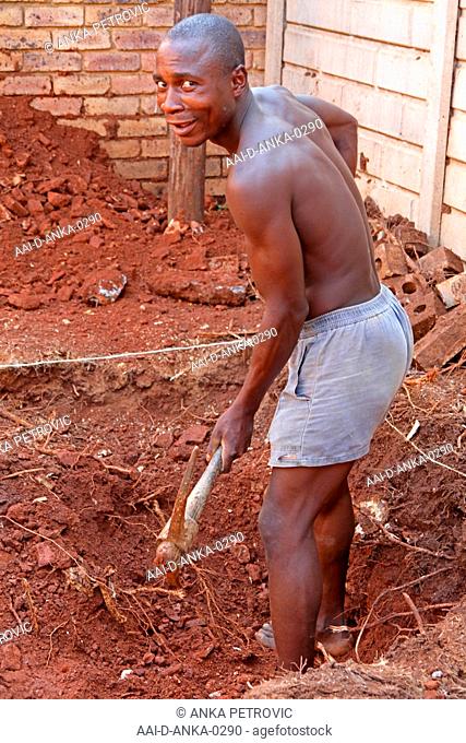 Construction worker with pick-axe digging a hole for a small swimming pool, Moreleta Park, Pretoria, Gauteng, South Africa