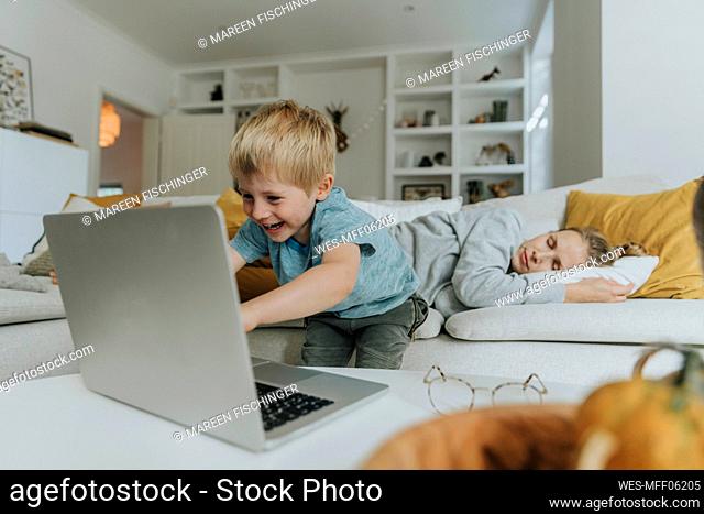 Boy using laptop by mother sleeping on sofa at home