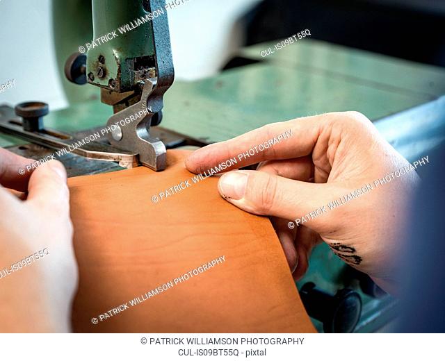 Leatherworker using machining leather handbag edge in workshop, close up of hands