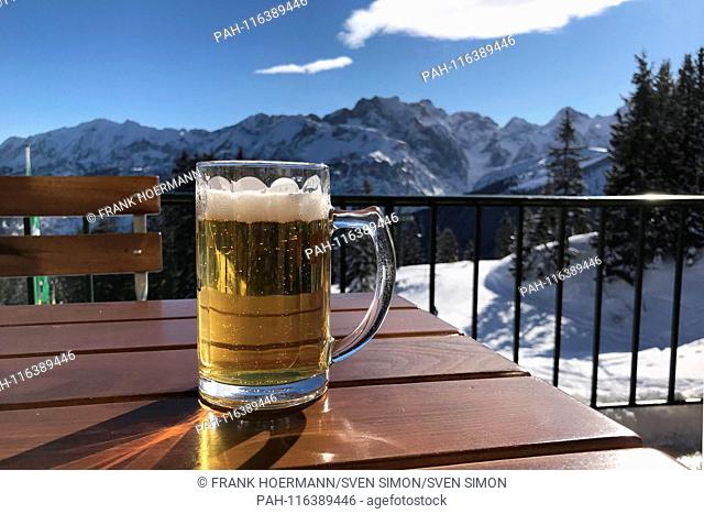 a cool fresh beer is standing on a wooden table on the terrace of the Kreuzeckhaus. Alcohol. Skiers in the Bavarian Alps, Garmisch Classic ski resort