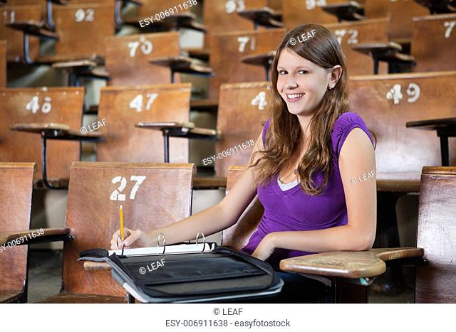 Portrait of young woman in lecture hall writing in binder