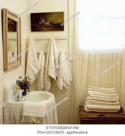 Cream towels on pegboard in cottage bathroom with white curtain below basin and lace curtain on window