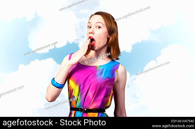 Surprised young female model with red hair. Shocked european woman hiding open mouth behind hand and feeling amazed. Elegant flirty lady in colorful dress and...