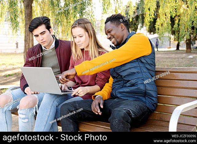 Friends sitting on park bench sharing laptop