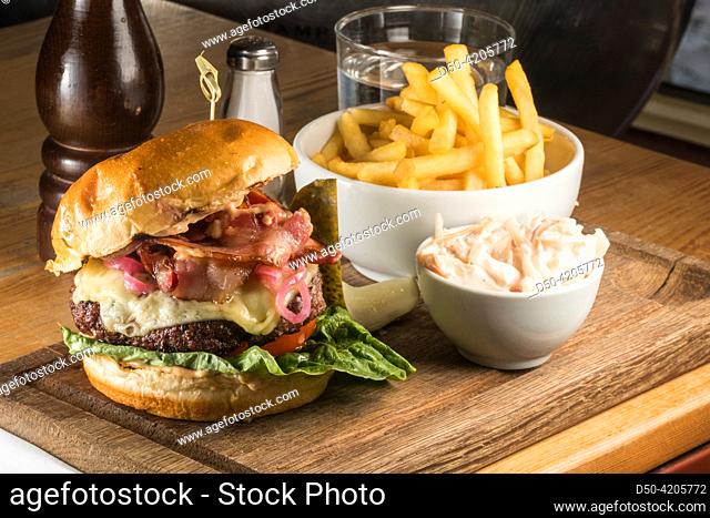 A cheeseburger with bacon, french fries and coleslaw on a wooden board