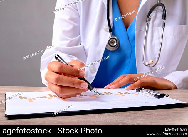 Mid section of female doctor writing on clipboard against grey background