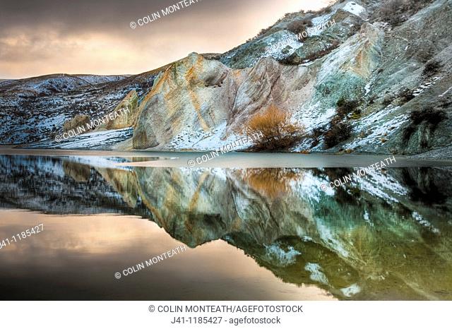 Blue Lake reflections of clay cliffs after winter storm and snowfall, St Bathans, Central Otago, New Zealand