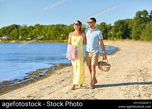 happy couple with picnic basket walking on beach