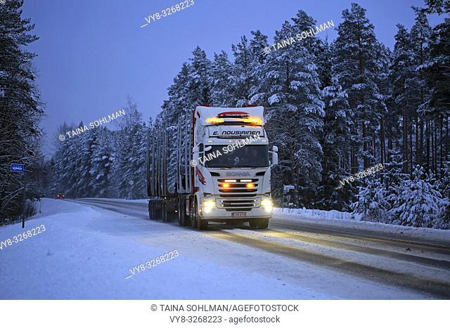 Salo, Finland - January 25, 2019: Scania R520 logging truck of E Nousiainen lights up rural highway in the blue hour of winter dusk
