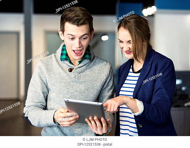 Two young millennial business professionals surpirsed by what they see on the tablet at their place of work; Sherwook Park, Alberta, Canada