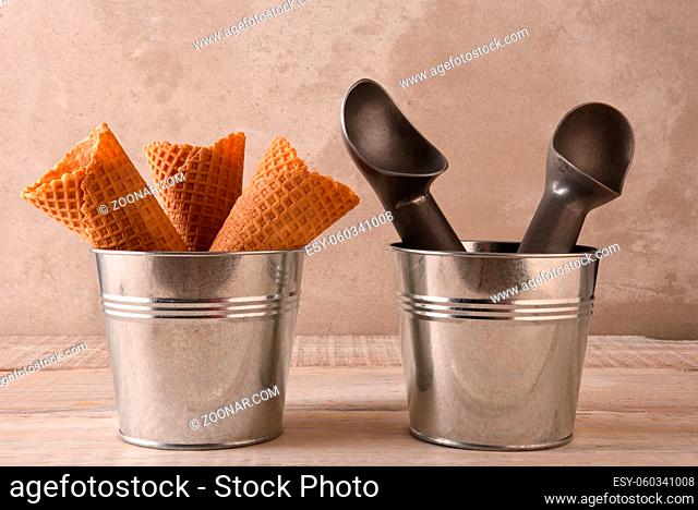 Closeup of three ice cream cones in a small metal bucket next to a pail with two scoops
